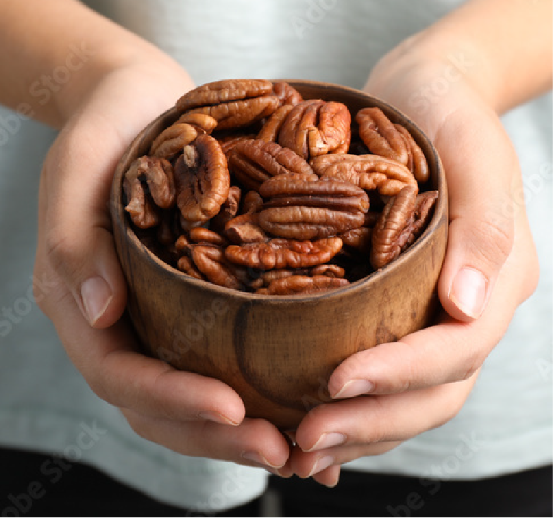 A person holding a small wooden bowl filled with pecan nuts in both hands.